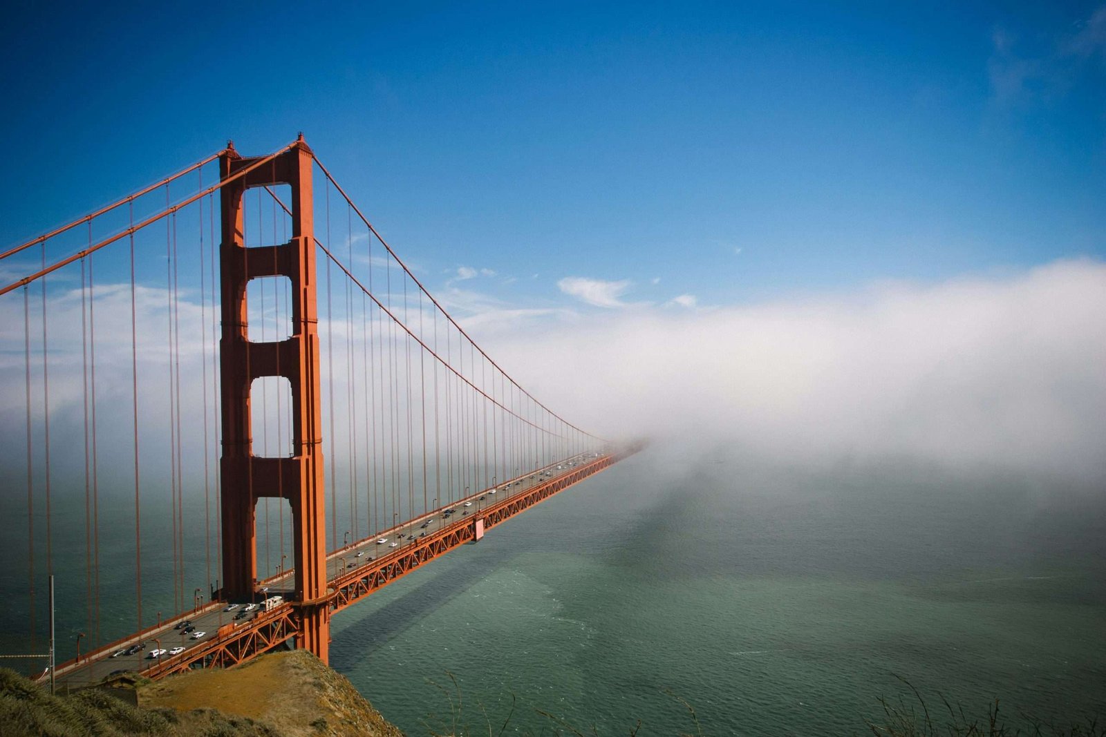 Stunning view of Golden Gate Bridge partially covered by fog with clear blue sky.